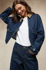 Sobrecamisa de denim azul oscuro, con cuello de pana color camel, cierre frontal de cremallera y dos bolsillos frontales con tapa y botón.