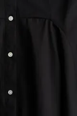 Vestido corto negro de algodón con escote redondo, manga japonesa, botonadura frontal y cintura entallada con pinzas. Falda acampanada con inserciones para dar volumen.