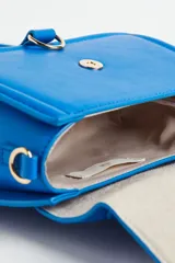 Cartera bandolera azul eléctrico de cuero sintético, con asa corta superior y correa larga extraíble. Tiene solapa con cierre magnético y detalle de hebilla metálica dorada.