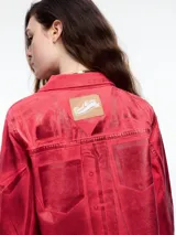 Campera corta de denim color rojo con textura metalizada, cuello camisero, cierre frontal con botones a presión, bolsillos de parche en el pecho y ruedo desflecado.