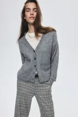 Cárdigan de punto gris jaspeado, con cuello en V, botones frontales y dos bolsillos delanteros abiertos. Presenta un corte holgado y hombros caídos, con puños y bajo acanalados.