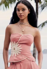 Top strapless rosa coral con silueta peplum y flor tejida artesanal en el frente. Presenta bordes delineados en crochet crudo.