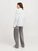 Camisa blanca de corte oversize con cuello clásico, cierre frontal con botones y pequeños brillantes plateados distribuidos por toda la prenda.