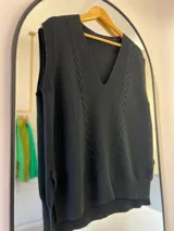 Chaleco negro de hilo con escote en pico, punto elástico en mangas y bajo, detalle de punto elástico y punto en ocho en la parte delantera.