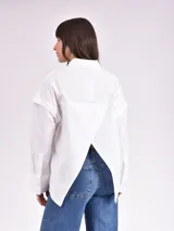 Camisa celeste de corte amplio, con cuello clásico, cierre frontal con botones, bolsillo en el pecho y mangas largas con detalle de botones en los puños.