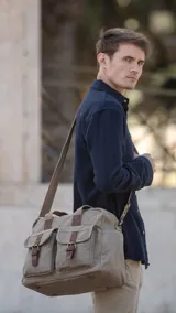Bolso tipo duffel de lona color beige con detalles en cuero marrón. Tiene doble asa de mano y correa bandolera ajustable y desmontable. Cuenta con cierre superior, bolsillos frontales con hebilla y bolsillos internos.