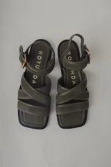 Sandalia plana de cuero color verde militar, con tiras cruzadas en el empeine y una tira ajustable con hebilla metálica dorada en el tobillo.