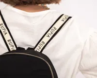 Mochila negra de nylon con cierres metálicos, grifa de goma con logo RUPIA, detalles de cordones combinados, bolsillos internos y externos, y correa regulable.
