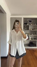 Camisa blanca de muselina con cuello clásico, corte holgado y mangas largas con puños abotonados.