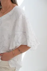 Blusa blanca de lino con escote en V, mangas cortas amplias y estampado floral en relieve.