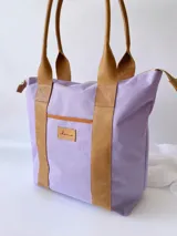 Bolso tipo tote de lona color fucsia con asas de cuero marrón, bolsillo interno y externo.