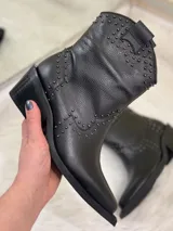 Botas cortas negras de cuero con punta fina, taco cuadrado y apliques de tachas plateadas.