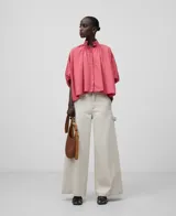 Camisa amplia de algodón color rosa, con cuello mao fruncido y bordado a tono. Manga corta con puño fruncido, botonadura frontal oculta con bordado a tono, bajo asimétrico y pliegue en la espalda.
