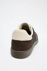 Zapatillas deportivas marrones con detalles en color crema y suela plana.
