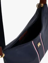 Bolso de hombro tipo hobo de nailon color azul marino, con correa de hombro ajustable de tela azul marino y detalles en cuero marrón. Presenta una franja vertical central con ribetes rojos y blancos, y un monograma TH dorado en el centro.