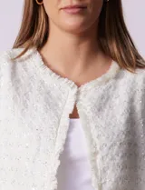 Chaqueta cruda de tejido boucle con flecos en el borde y botones negros en los puños.