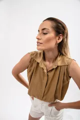 Camisa color marrón claro sin mangas, con cuello camisero y cierre frontal con botones.