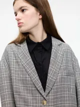 Blazer gris a cuadros con solapas de muesca, cierre con dos botones y corte holgado. Incluye un prendedor de flor negra en la solapa.