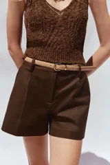 Bermuda color crema de tiro medio con pinzas delanteras y cinturón fino color beige. Tiene bolsillos frontales y falsos bolsillos de vivo en la espalda.