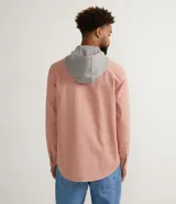 Camisa overshirt color salmón de sarga de algodón con capucha gris ajustable con cordones. Tiene cierre frontal con botones, dos bolsillos con solapa en el pecho y mangas largas con puños abotonados.