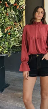 Blusa color beige de corte holgado, cuello alto con volados y mangas largas abullonadas con elástico en los puños.