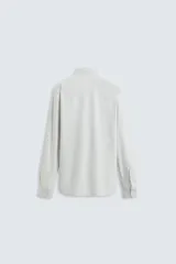 Camisa celeste a rayas verticales blancas, de corte recto, con cuello italiano abierto, mangas largas con puños abotonados y cierre frontal con botones.