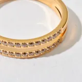 Anillo dorado de acero con dos filas de piedras brillantes en el centro.