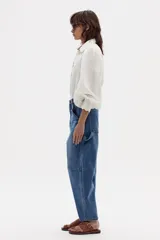 Camisa blanca de lino con estampado de cuadros azules y marrones, cuello camisero clásico, mangas largas abullonadas con puños elásticos, botones de nácar frontales y ruedo curvo.