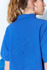 Camisa celeste de manga corta con cuello clásico, cierre frontal con botones y bordados ondulados en el frente.