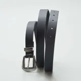 Cinturón fino negro de cuero sintético con hebilla metálica plateada estilo western.