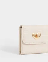 Billetera pequeña color crema con textura croco, solapa con broche dorado en forma de corazón y múltiples compartimentos para tarjetas y billetes.