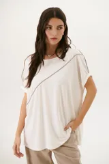 Remera negra de corte holgado con cuello redondo y mangas cortas con dobladillo. Presenta una línea diagonal blanca que cruza el frente desde el hombro hasta la cadera.