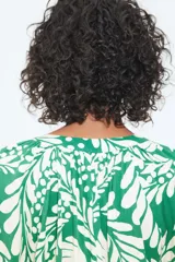 Blusa de tejido liviano color verde con estampado de hojas blancas, cuello corto fruncido y tapeta de botones. Mangas globo largas con volumen de corte raglán y puños finos abotonados.