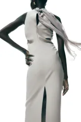 Vestido midi color gris topo, de cuello halter con lazada combinada a tono. Bajo con abertura en espalda. Cierre en espalda con cremallera, abertura y botón.