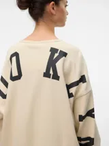 Sudadera oversize color crema con cuello redondo, hombros caídos, puños acanalados y estampado en el frente con la frase "New York City Brooklyn 1896". Tiene letras estampadas en las mangas.