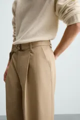 Pantalón negro de corte amplio con cinturón de tela con hebilla metálica. Presenta pliegues frontales, bolsillos laterales y traseros. Cierre frontal con cremallera y botón.
