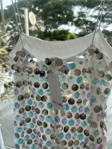 Vestido largo blanco tipo tubo cubierto de lentejuelas tornasoladas y plateadas, con tirantes finos y cierre en la espalda.