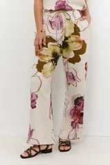 Pantalón de lino color celeste con estampado de flores grandes en tonos marrones, azules y rojos. El pantalón es de corte ancho y tiene cintura alta con cordón ajustable.