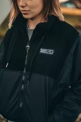 Campera negra con paneles de tela lisa y de corderito, cierre frontal con cremallera y cuello alto.