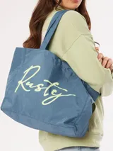 Bolso tipo tote bag de tela azul con estampado grande en cursiva de la marca "Rusty" en color verde claro.