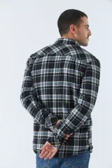 Sobrecamisa de algodón para hombre con interior de corderito, estampado a cuadros en tonos negro, blanco y azul. Tiene cierre de botones, bolsillos tipo cartera y logo en goma. El modelo usa talle M.