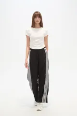 Pantalón de algodón negro, holgado, de calce medio, con cintura elástica y cordón ajustable. Presenta tres rayas blancas verticales en los laterales.