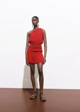 Vestido corto rojo de un solo hombro, con volados en el escote, cintura elastizada con cinturón de cadena dorada y falda con frunces.