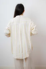 Conjunto de camisa y top corto a rayas verticales amarillas y blancas. El top es corto con tiras finas y elástico en la base. La camisa es de manga larga y corte relajado.