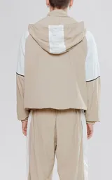 Anorak unisex beige y blanco con capucha, cierre parcial con cremallera, bolsillo tipo canguro con solapa y cordones ajustables con texto en la capucha.