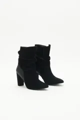 Botas de caña media de gamuza negra, con taco cuadrado y punta fina. Presenta tiras terminadas con borlas que se cruzan y atan alrededor de la caña.