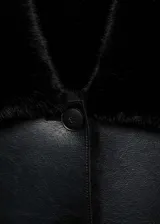 Chaqueta corta negra de cuero sintético con cuello y puños de piel sintética. Cierre frontal con botones y bolsillos de parche.
