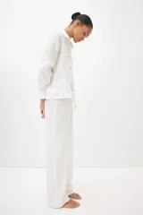 Conjunto de pijama de dos piezas en muselina de algodón suave color blanco con estampado floral. Incluye camisa de manga larga con cuello, botones y bolsillo superior, y pantalón recto con cintura elástica y cordón ajustable.