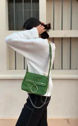 Cartera bandolera negra de ecocuero con textura arrugada, tachas plateadas, cadena decorativa y aro metálico.