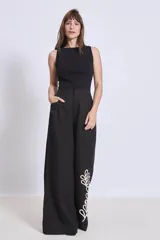 Pantalón negro de corte palazzo con apliques bordados en color crema en la parte inferior de una pierna.